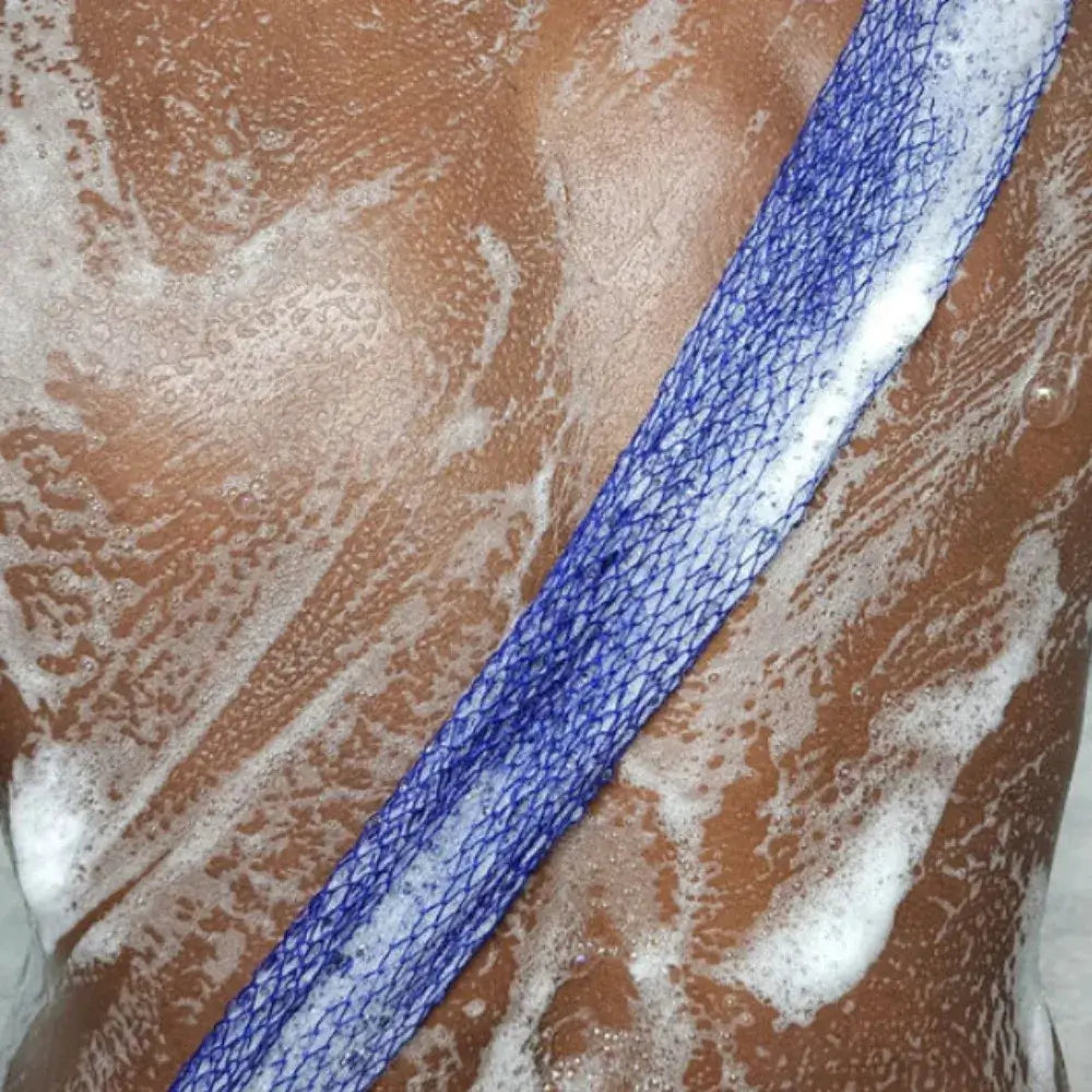 Close-up of a back being scrubbed with a blue exfoliating net sponge lathered with soap, showcasing effective cleansing.