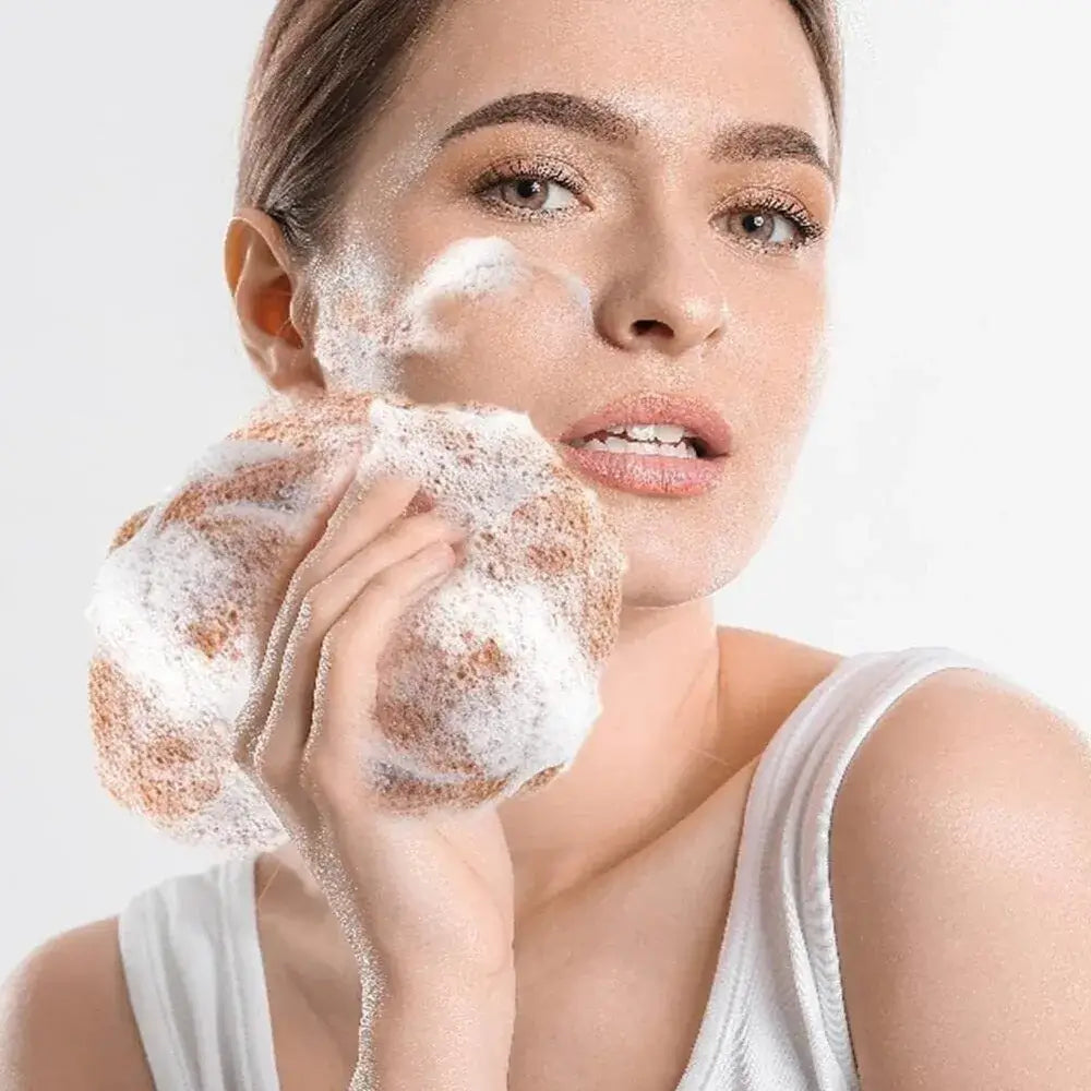 Woman using exfoliating net sponge with foam on her face for smoother skin.