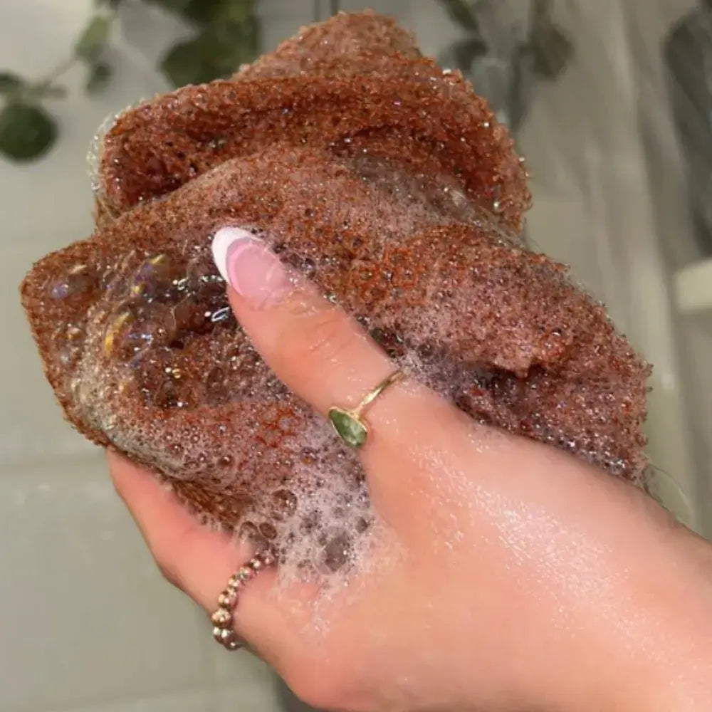 Hand holding a wet Exfoliating Mesh African Exfoliating Net Sponge creating rich foam for smoother skin.